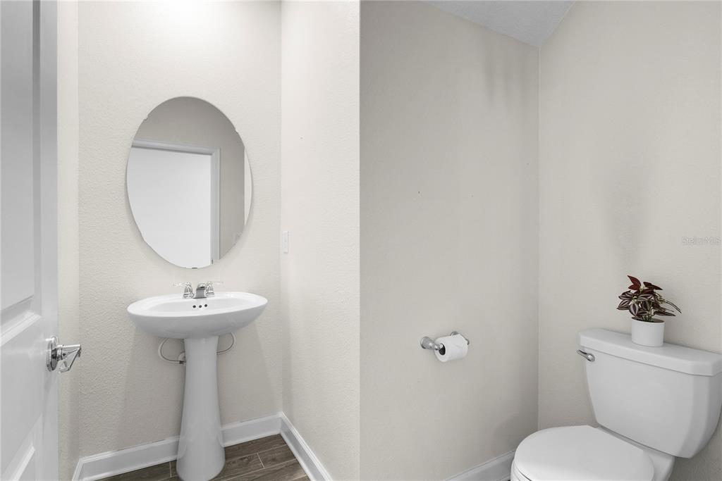 A powder room features a pedestal sink, oval mirror, toilet, and wood-look flooring — 144 TAFT DRIVE, DAVENPORT, FL