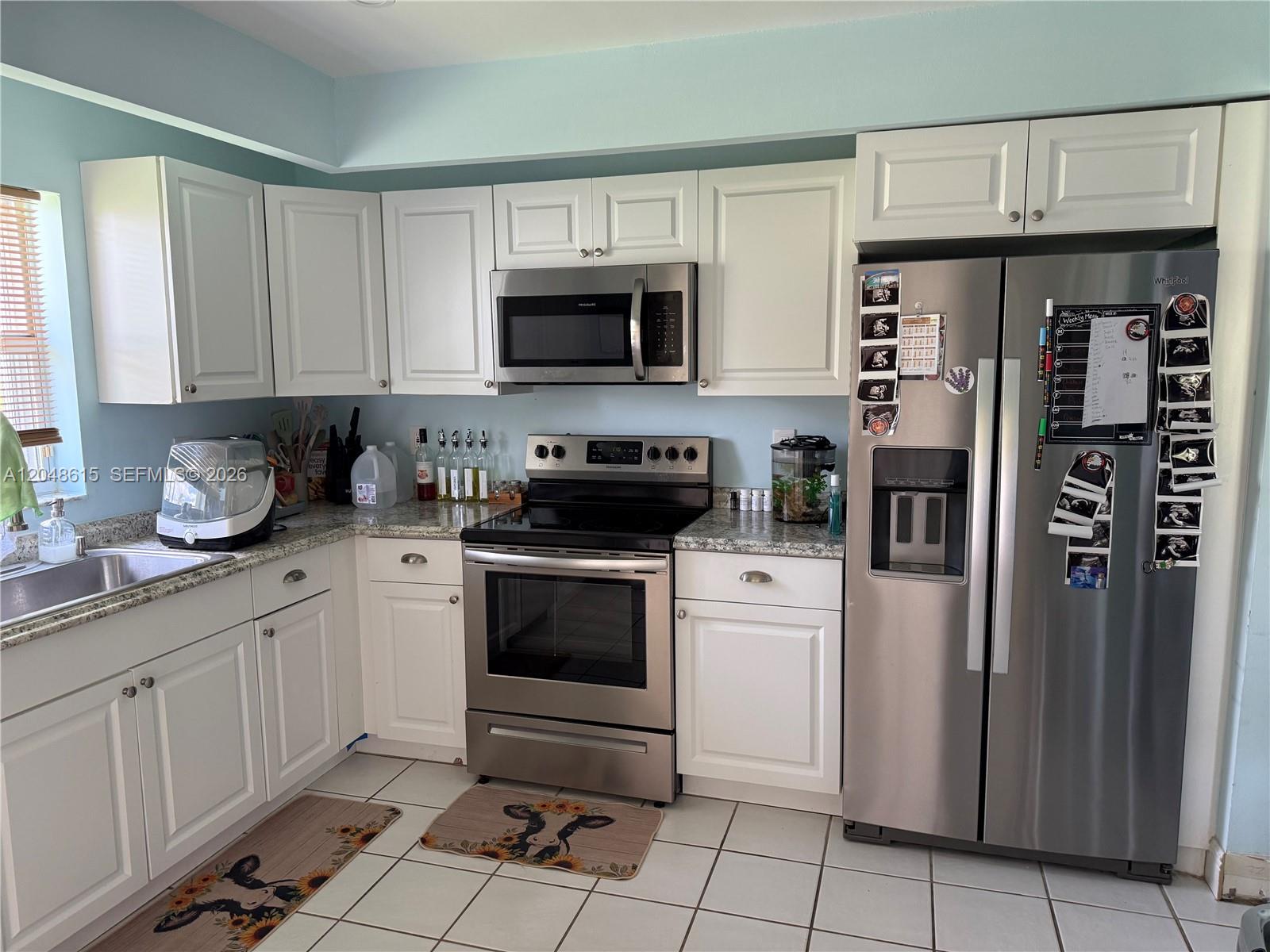 A kitchen features white cabinets, stainless steel appliances, granite countertops, and light blue walls — 2225 SE 5th Pl, Homestead FL 33033, HOMESTEAD, FL