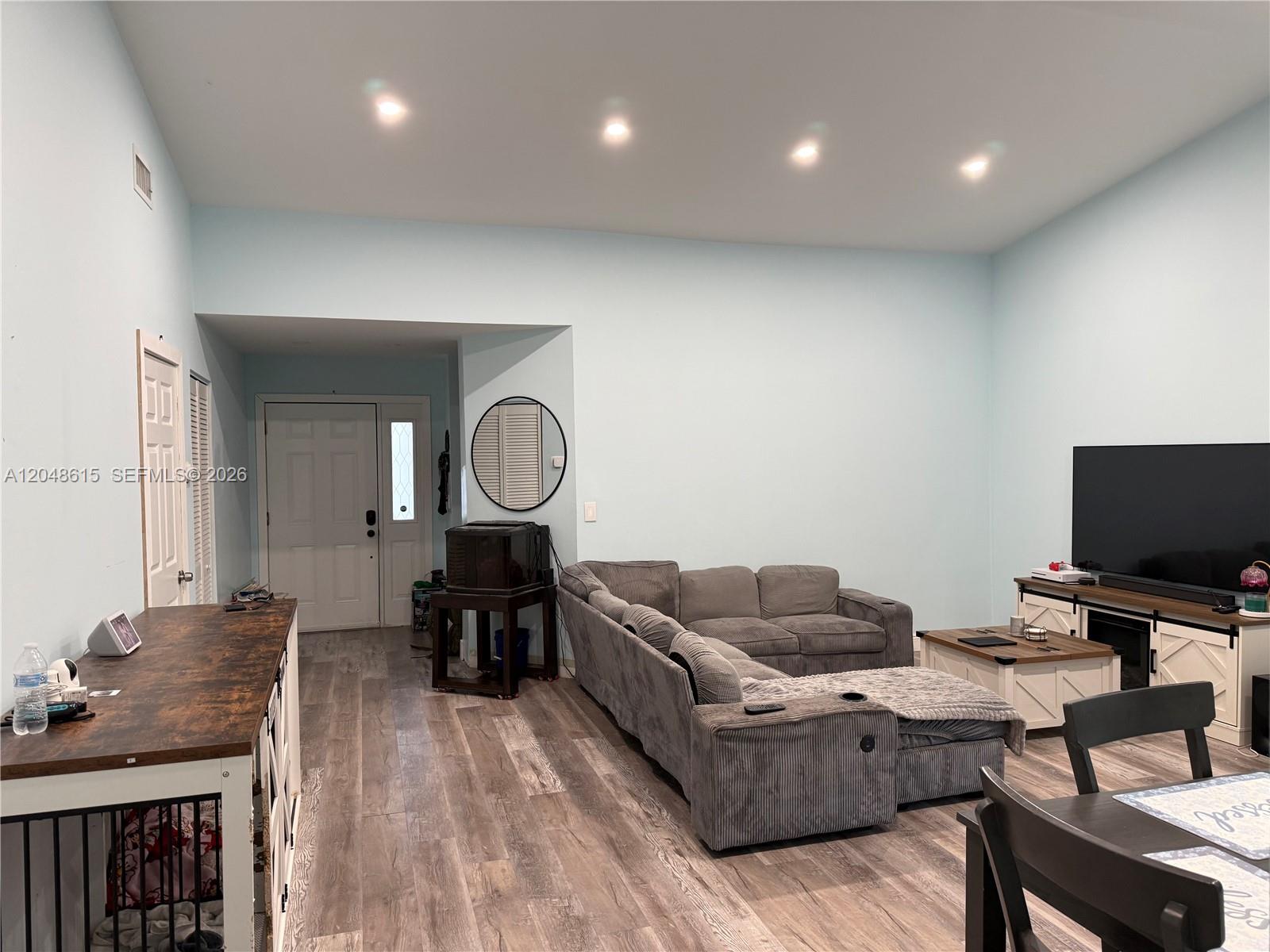 A living room features light blue walls, wood-look flooring, a gray sectional sofa, and a television — 2225 SE 5th Pl, Homestead FL 33033, HOMESTEAD, FL