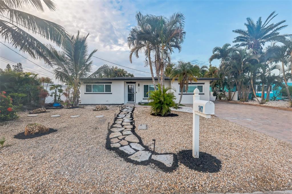 A single-story house with a stone walkway, gravel yard, and palm trees — 747 PRUITT DRIVE, MADEIRA BEACH, FL