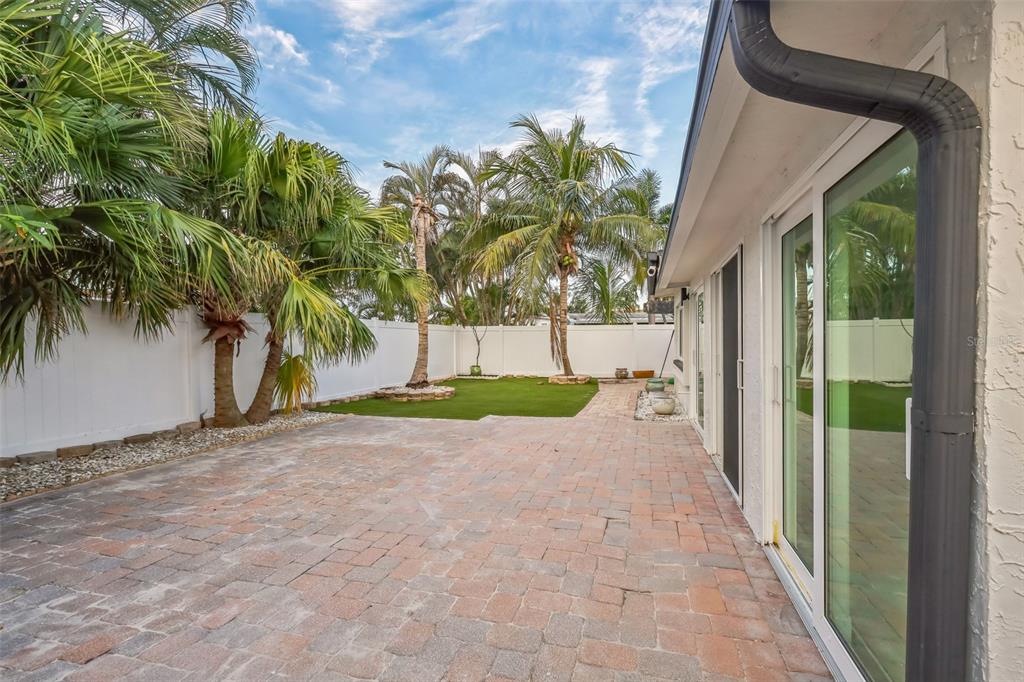 A paved patio leads to a small artificial turf lawn enclosed by a white fence — 747 PRUITT DRIVE, MADEIRA BEACH, FL