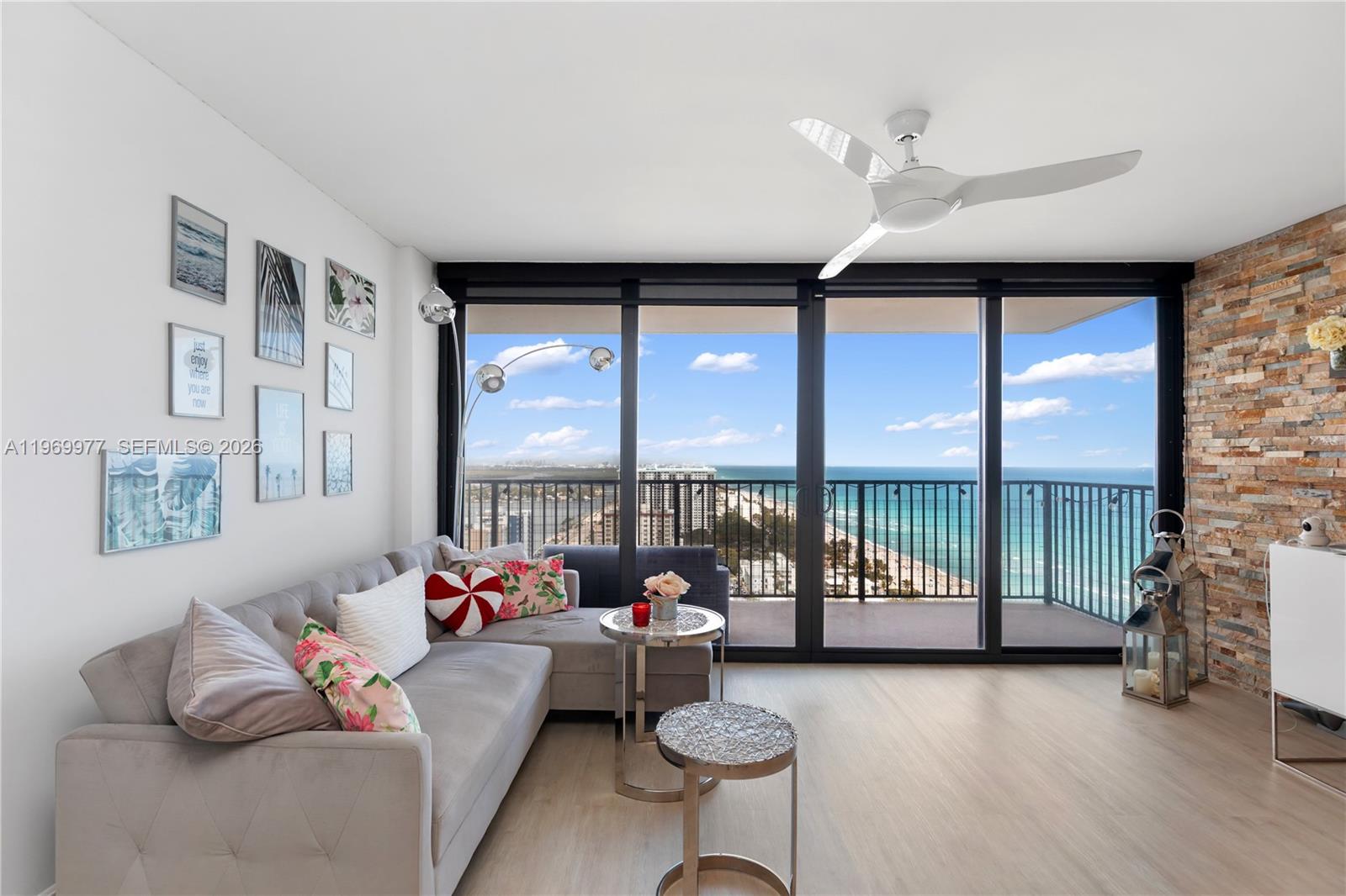 A living room features a gray sectional sofa, stone accent wall, and balcony with ocean views — 2101 S Ocean Dr # 2804, Hollywood FL 33019, HOLLYWOOD, FL