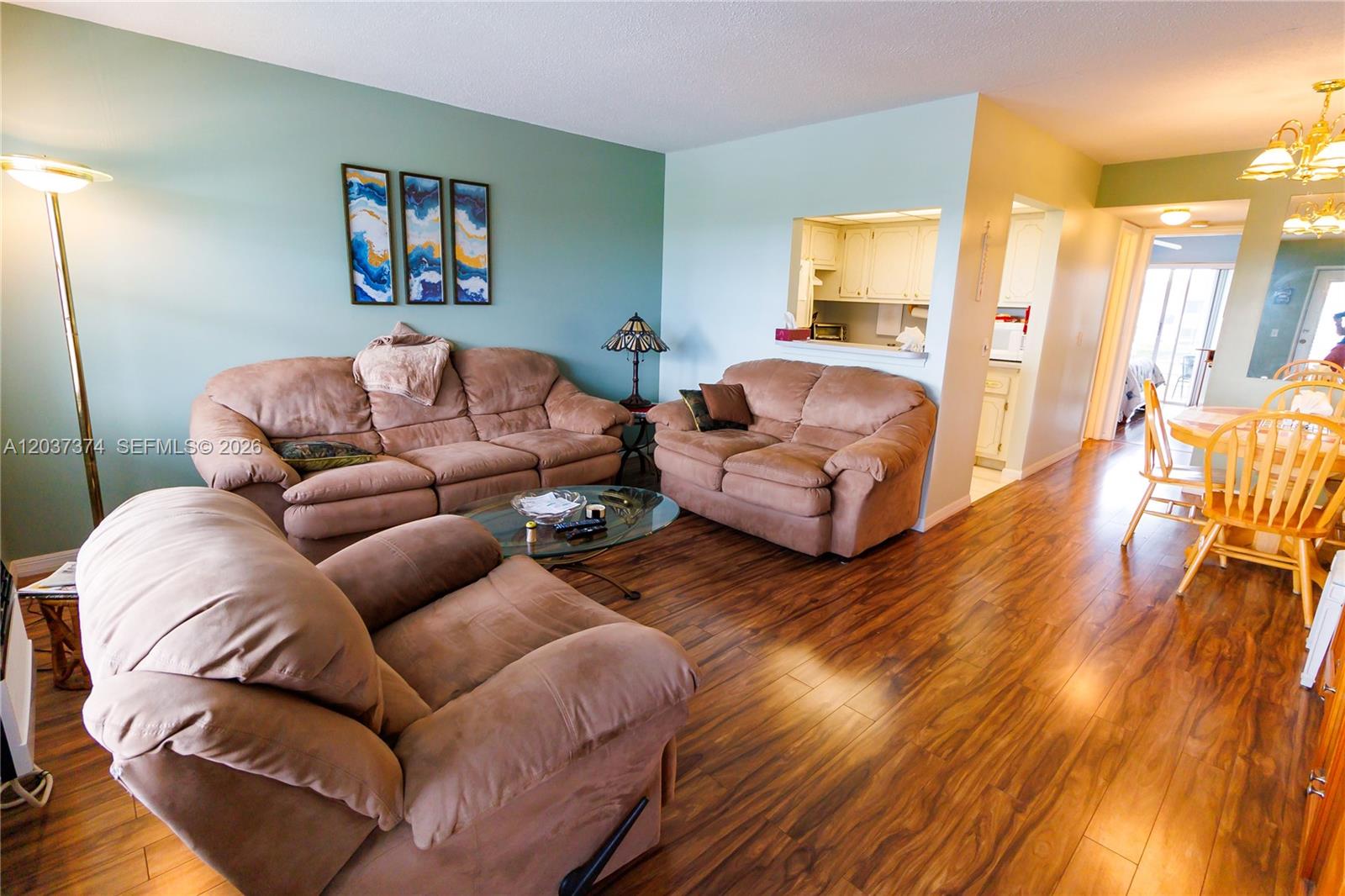 A living room features brown furniture, wood-look flooring, and a pass-through window to the kitchen — 90 Berkshire D # 90, West Palm Beach FL 33417, WEST PALM BEACH, FL