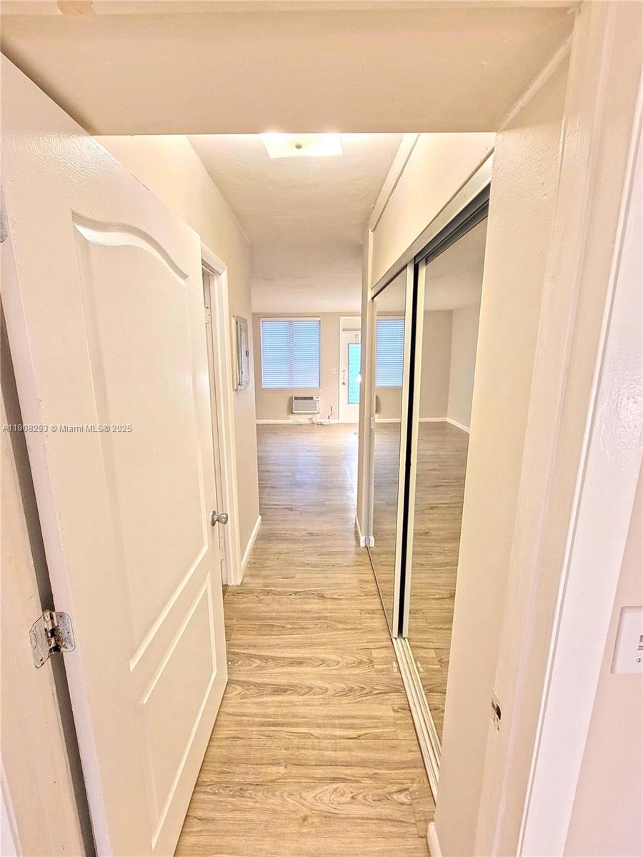 A hallway with light wood-look flooring leads to an open living area with mirrored closets — 441 Collins Ave # 12A, Miami Beach FL 33139, MIAMI BEACH, FL
