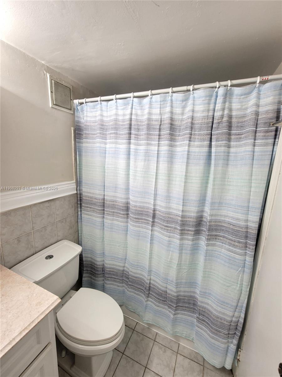 A bathroom features a white toilet, a striped shower curtain, and light-colored tile flooring — 441 Collins Ave # 12A, Miami Beach FL 33139, MIAMI BEACH, FL