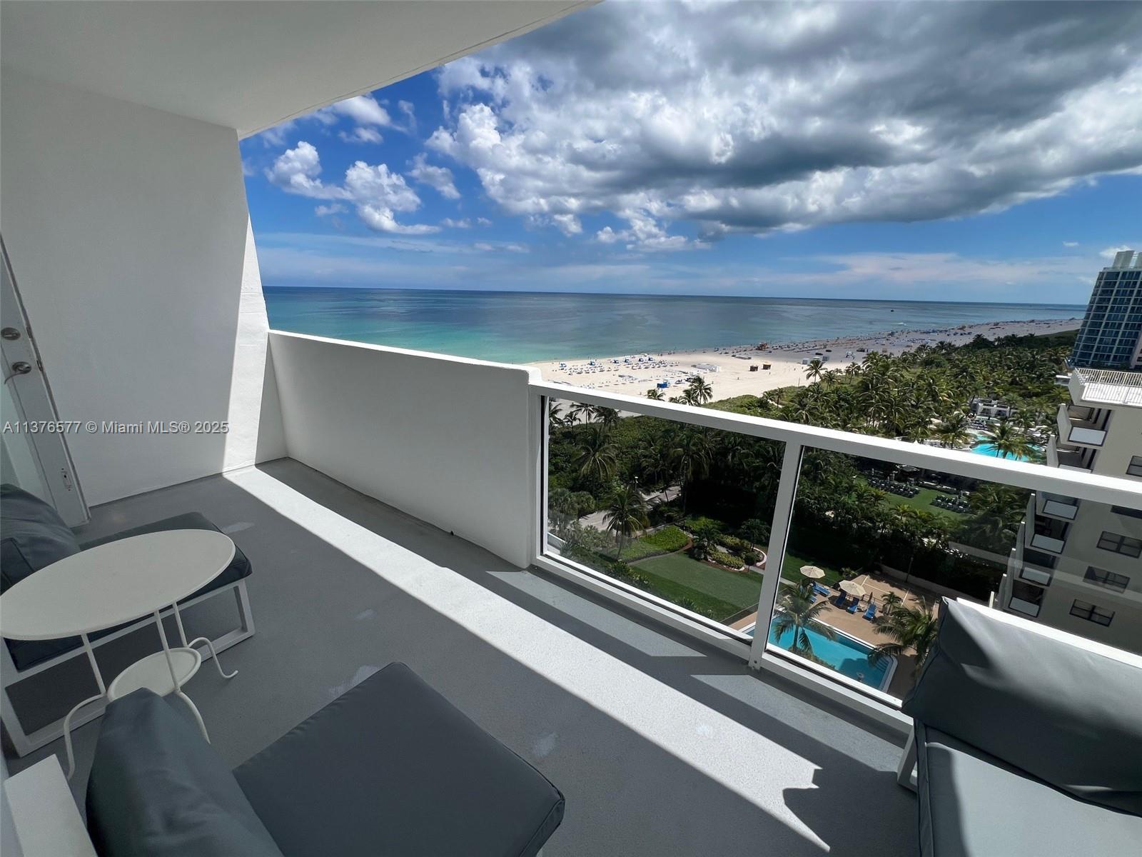 A balcony with outdoor furniture overlooks the ocean, beach, and a swimming pool below — 100 Lincoln Rd # 1244, Miami Beach FL 33139, MIAMI BEACH, FL