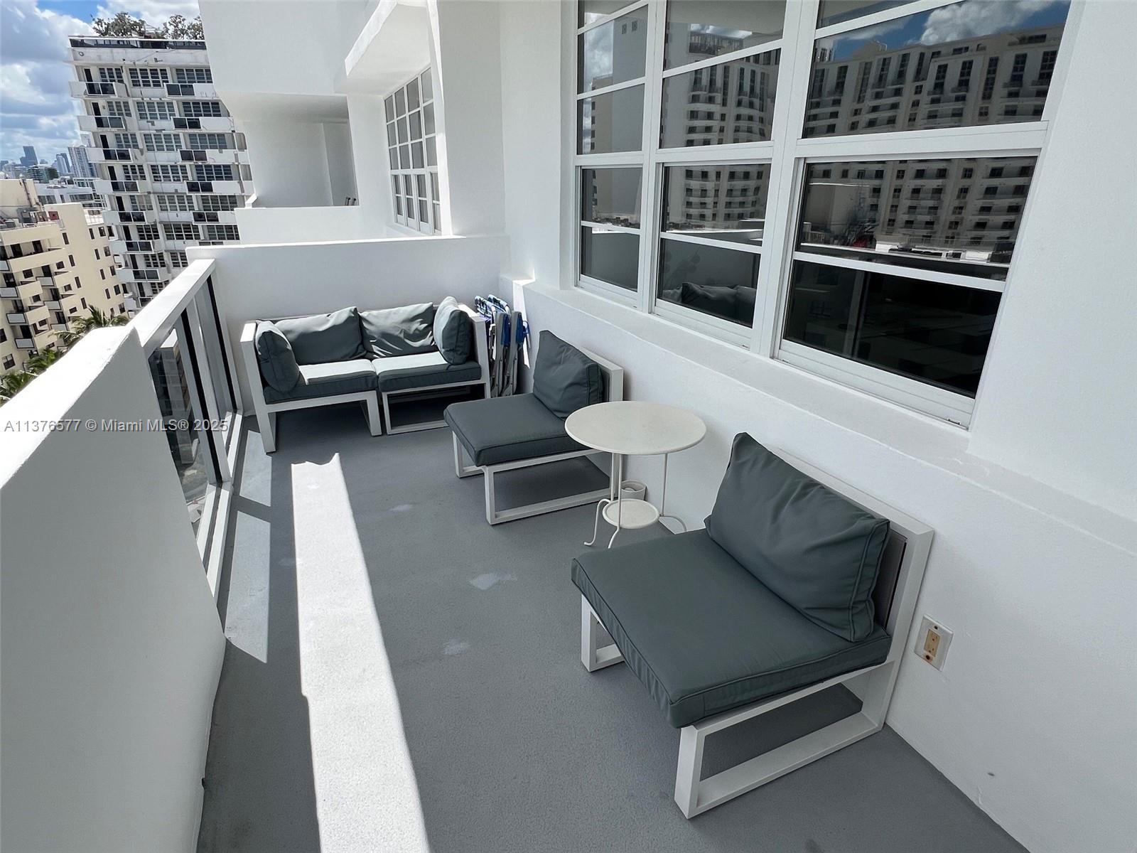 A balcony features white metal furniture with grey cushions and a small round table — 100 Lincoln Rd # 1244, Miami Beach FL 33139, MIAMI BEACH, FL