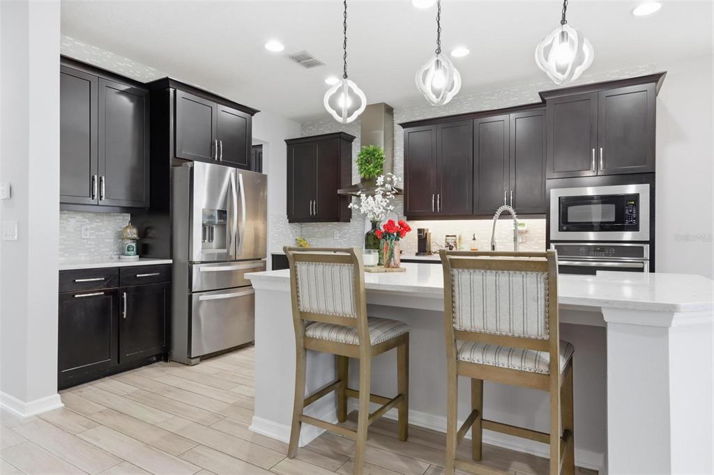 A modern kitchen features dark wood cabinets, stainless steel appliances, and a white quartz island — 297 ANCONA AVENUE, DEBARY, FL