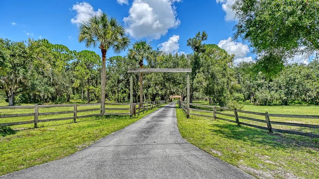 A paved driveway leads through a wooden gate toward a house surrounded by trees — 6455 MCKOWN ROAD, SARASOTA, FL