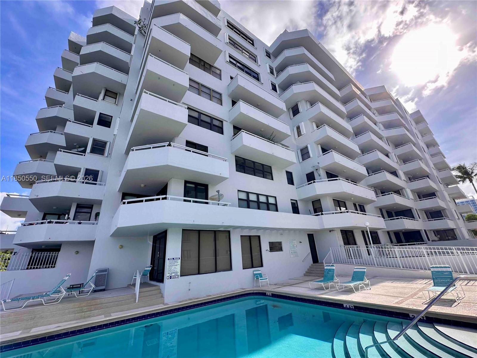 A low-angle view of a white multi-story apartment building with balconies overlooking a swimming pool — 6830 Indian Creek Dr # 6D, Miami Beach FL 33141, MIAMI BEACH, FL