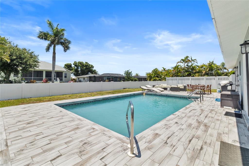 A backyard features a rectangular swimming pool surrounded by light-colored wood-look tile decking — 60 GOLFVIEW ROAD, ROTONDA WEST, FL