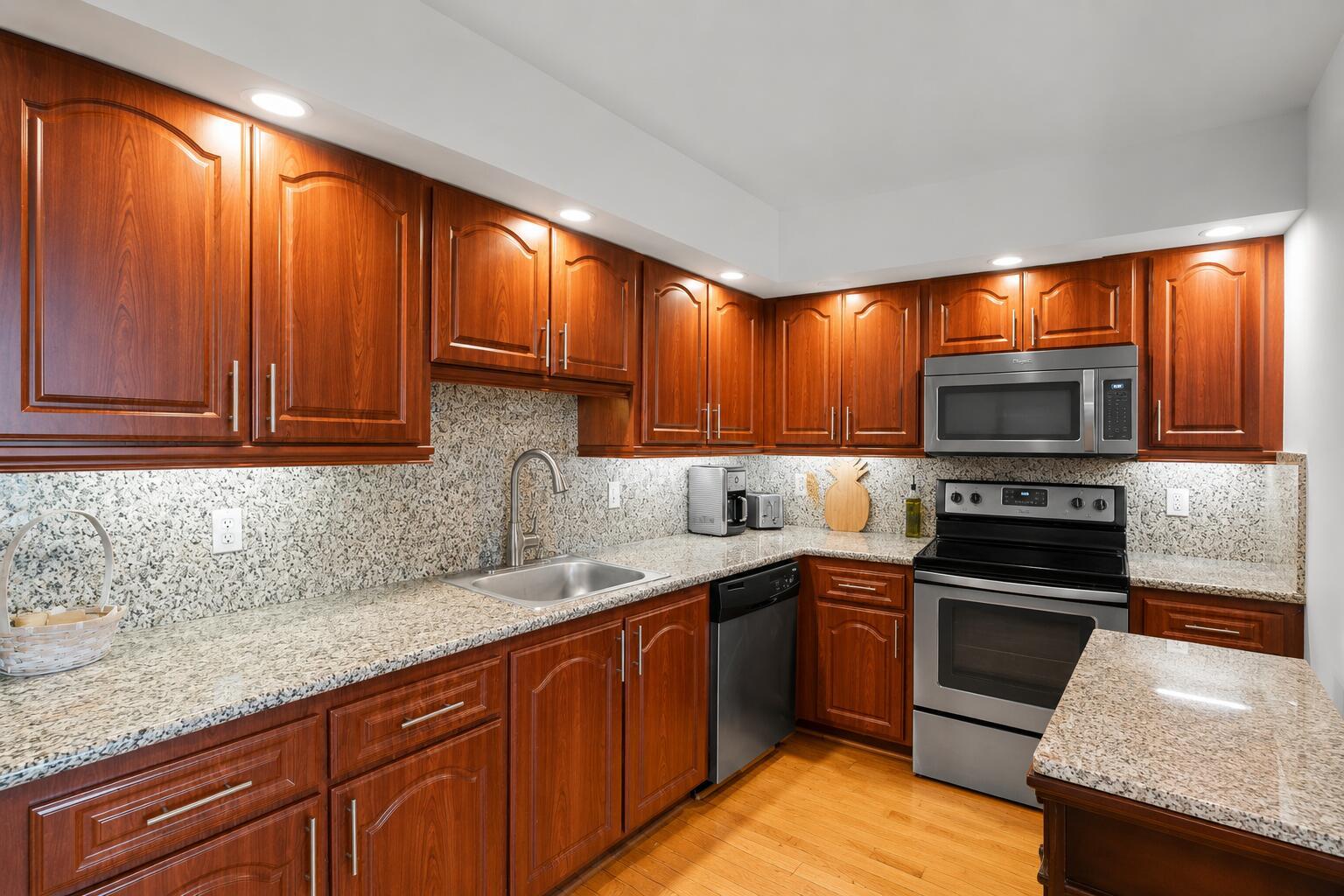 A kitchen features wood cabinets, granite countertops, stainless steel appliances, and light wood flooring — 625 Oaks Drive # 405, Pompano Beach FL 33069, POMPANO BEACH, FL