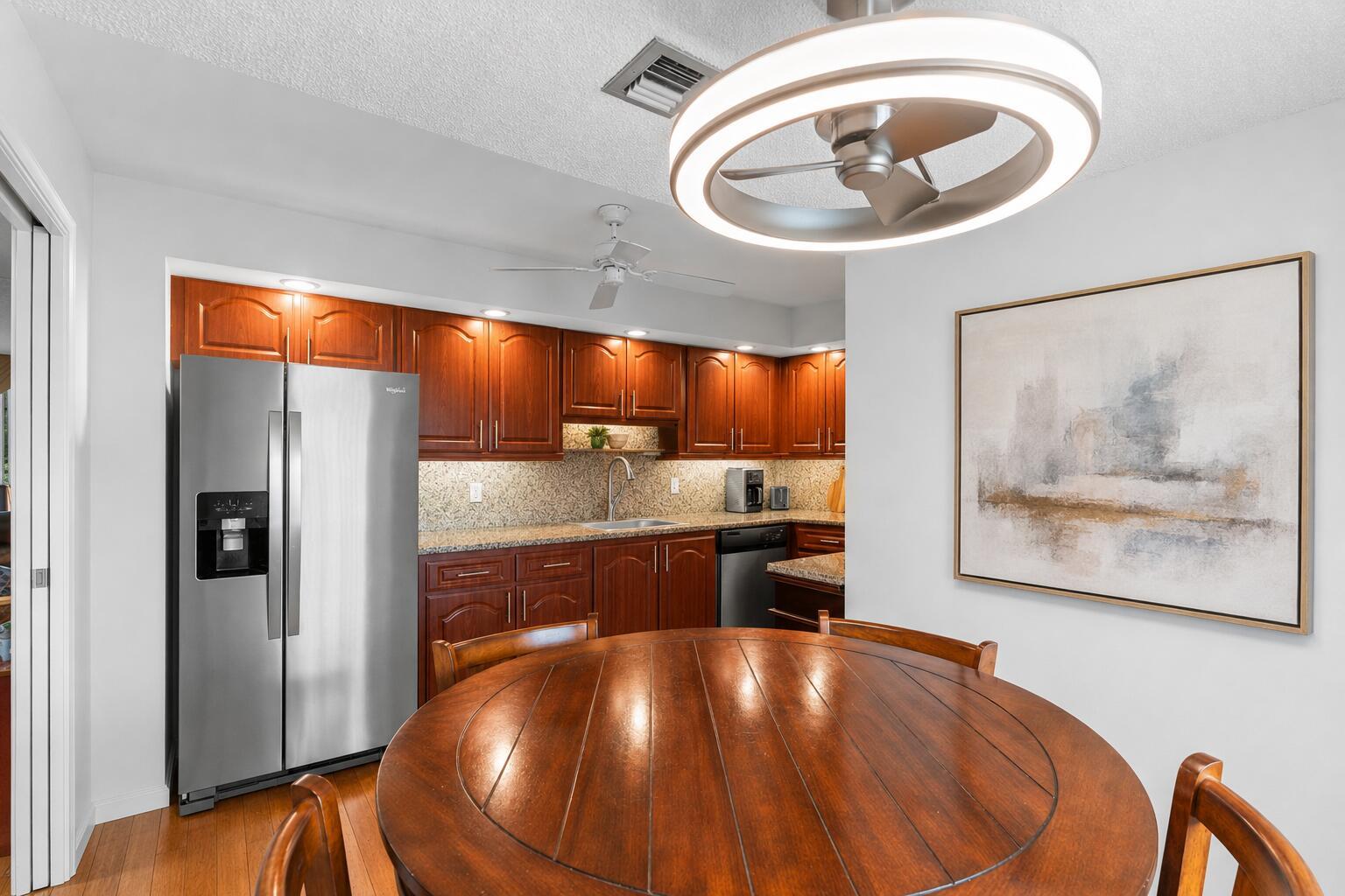A dining area with a round wooden table sits adjacent to a kitchen with wood cabinets — 625 Oaks Drive # 405, Pompano Beach FL 33069, POMPANO BEACH, FL