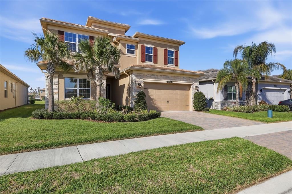 A two-story suburban house with a tan stucco exterior, stone accents, and a paved driveway — 32801 TREE OF LIFE AVENUE, WESLEY CHAPEL, FL
