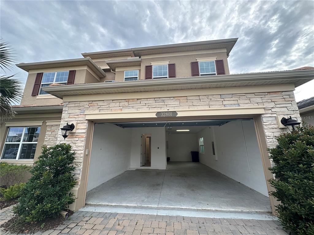 A two-story suburban house with a tan stucco exterior, stone accents, and a two-car garage — 32801 TREE OF LIFE AVENUE, WESLEY CHAPEL, FL