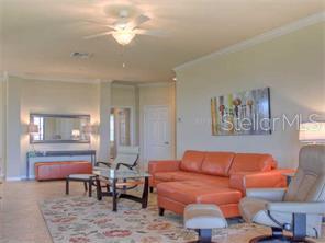 A living room features an orange sectional sofa, a patterned area rug, and a ceiling fan — 7112 GRAND ESTUARY TRAIL UNIT 103, BRADENTON, FL