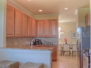 A kitchen with light wood cabinets, granite countertops, and a breakfast bar overlooking a dining area — 7112 GRAND ESTUARY TRAIL UNIT 103, BRADENTON, FL