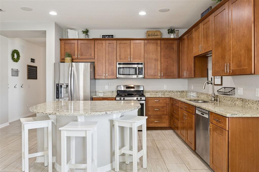 A kitchen with wood cabinets, granite countertops, stainless steel appliances, and a curved island — 12549 HAMMOCK POINTE CIRCLE, CLERMONT, FL