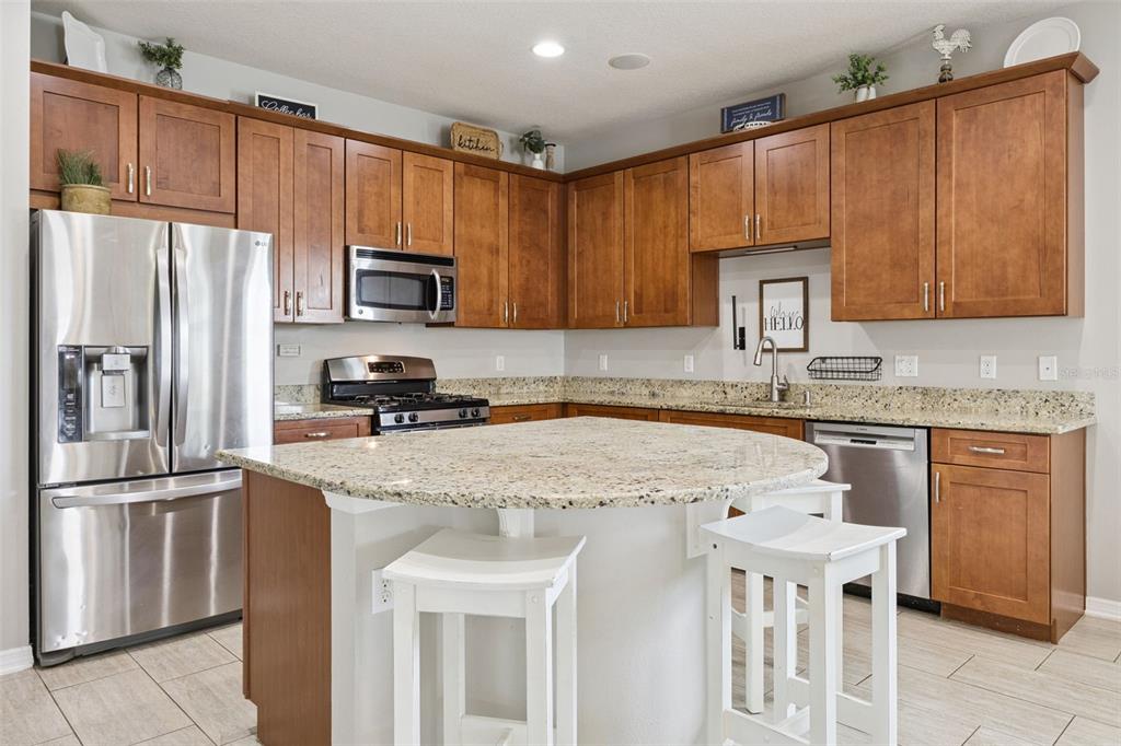 A kitchen features wood cabinets, granite countertops, stainless steel appliances, and a central island — 12549 HAMMOCK POINTE CIRCLE, CLERMONT, FL