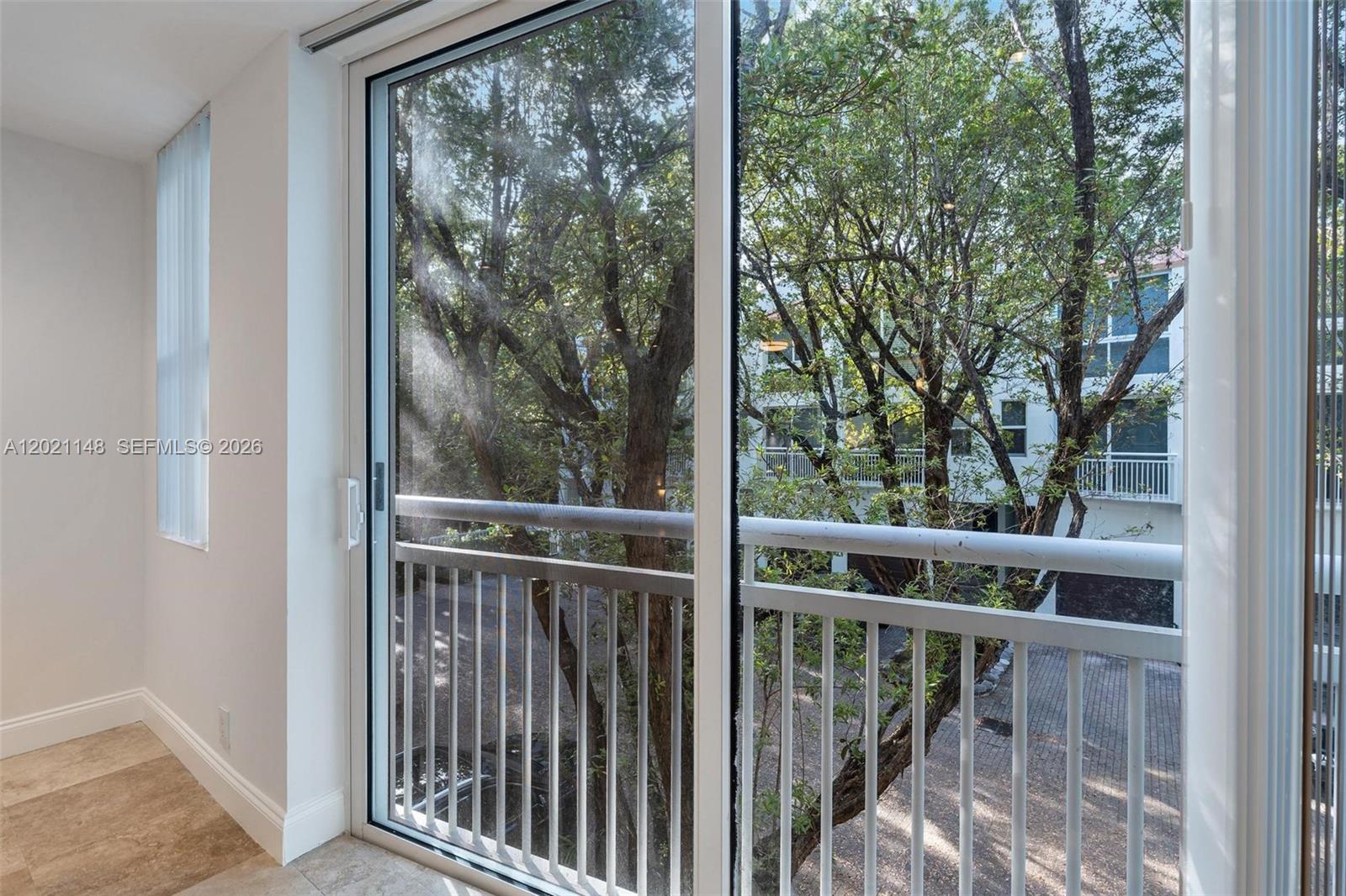 A sliding glass door opens to a balcony overlooking trees and a neighboring building — 325 Meridian Ave # 5, Miami Beach FL 33139, MIAMI BEACH, FL