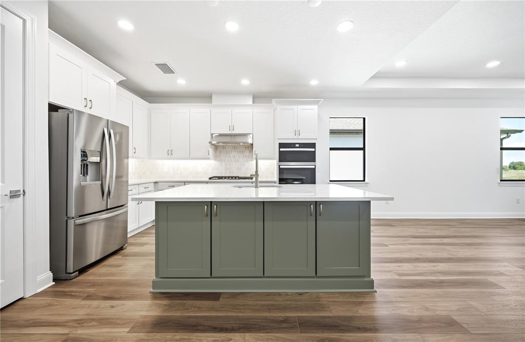 A modern kitchen features white cabinets, a sage green island, and stainless steel appliances — 5888 WINDBREAK COURT, APOLLO BEACH, FL