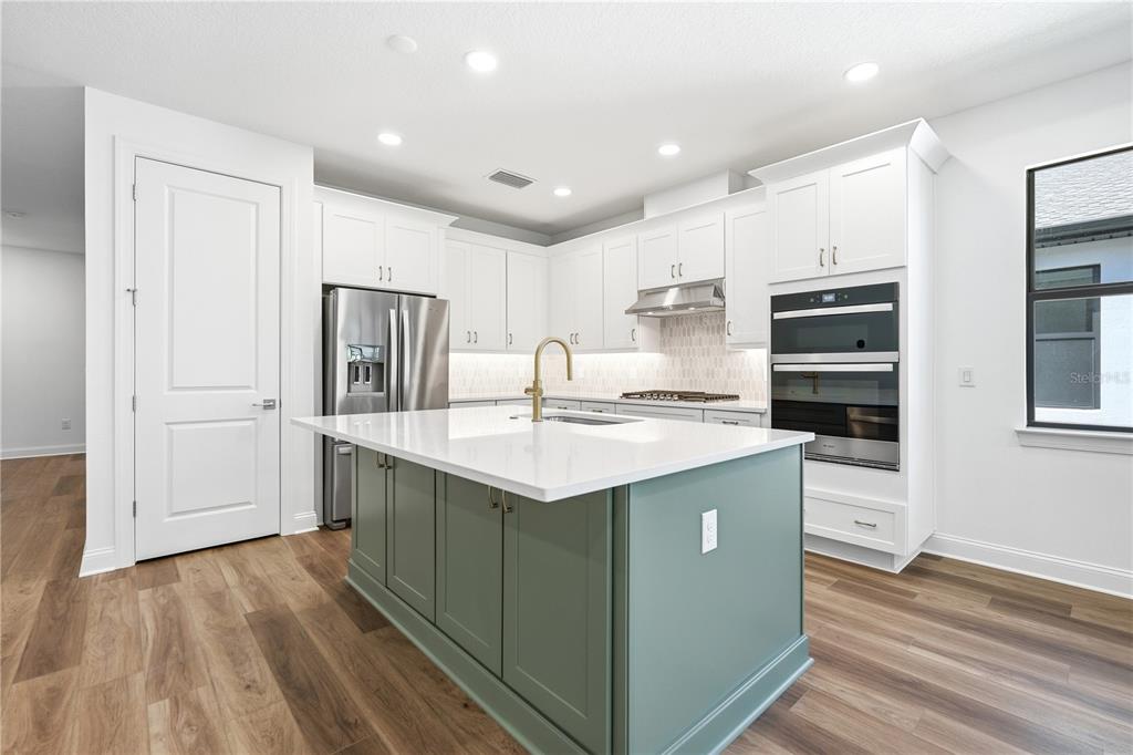 A modern kitchen features white cabinetry, a green island, stainless steel appliances, and wood flooring — 5888 WINDBREAK COURT, APOLLO BEACH, FL