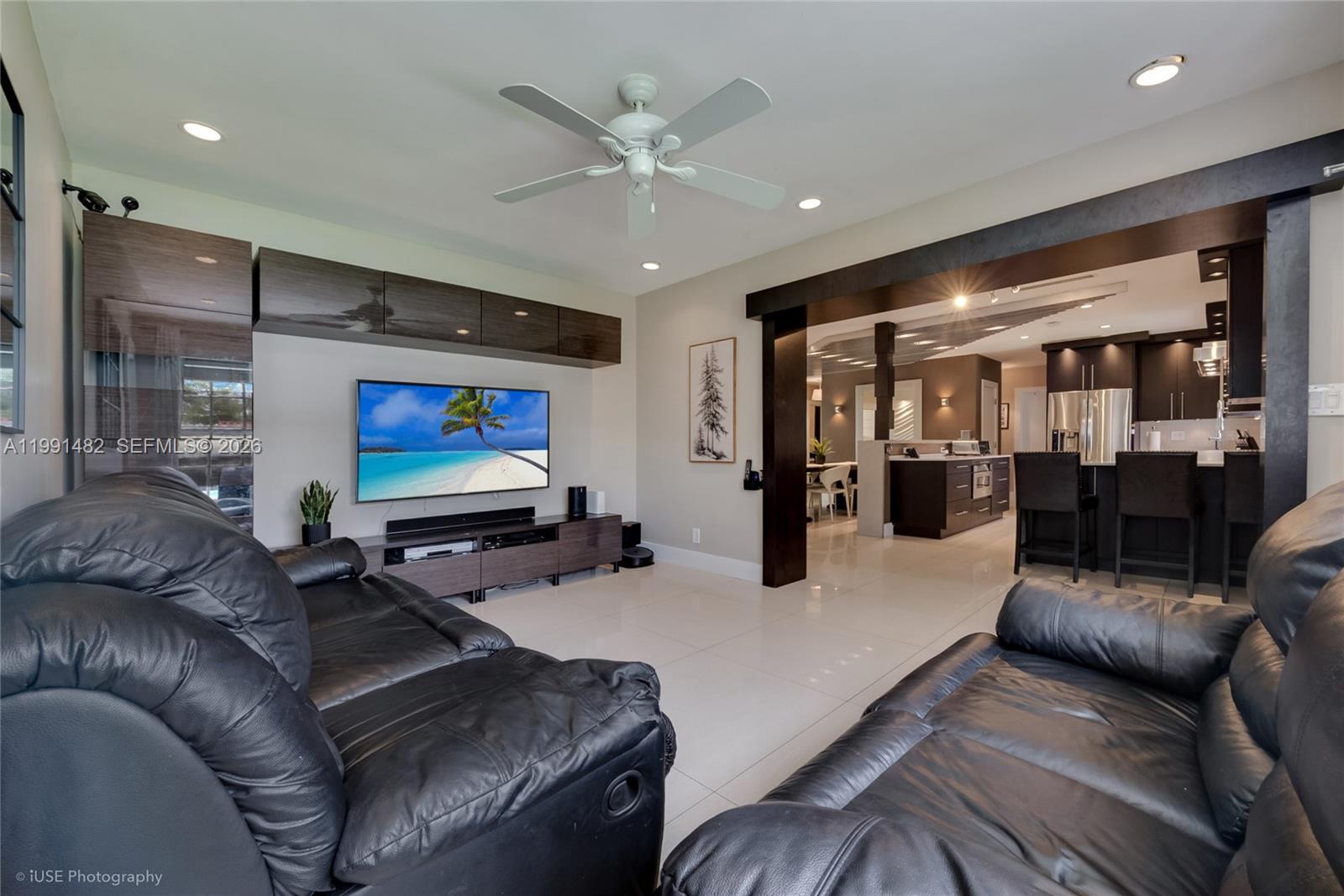 A living room with black leather sofas, a wall-mounted television, and an open kitchen — 7940 SW 20th Street, Miami FL 33155, MIAMI, FL