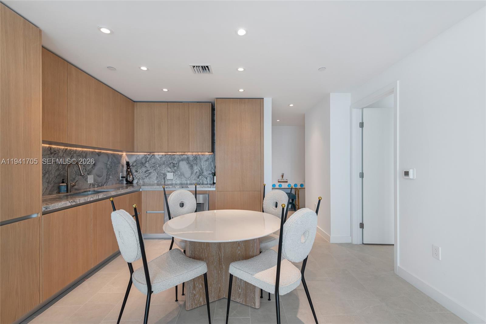 A modern kitchen features light wood cabinetry, marble countertops, and a round dining table — 500 Alton Rd # 1204, Miami Beach FL 33139, MIAMI BEACH, FL
