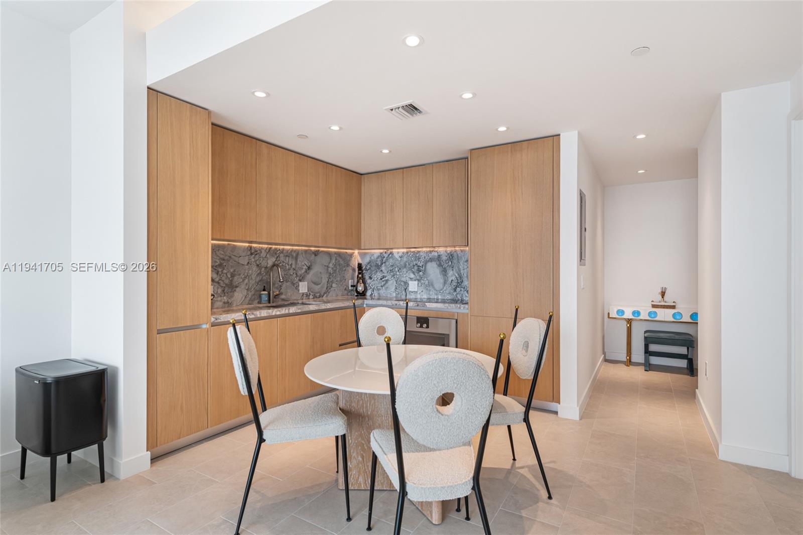 A modern kitchen features light wood cabinetry, marble backsplash, and a round dining table — 500 Alton Rd # 1204, Miami Beach FL 33139, MIAMI BEACH, FL
