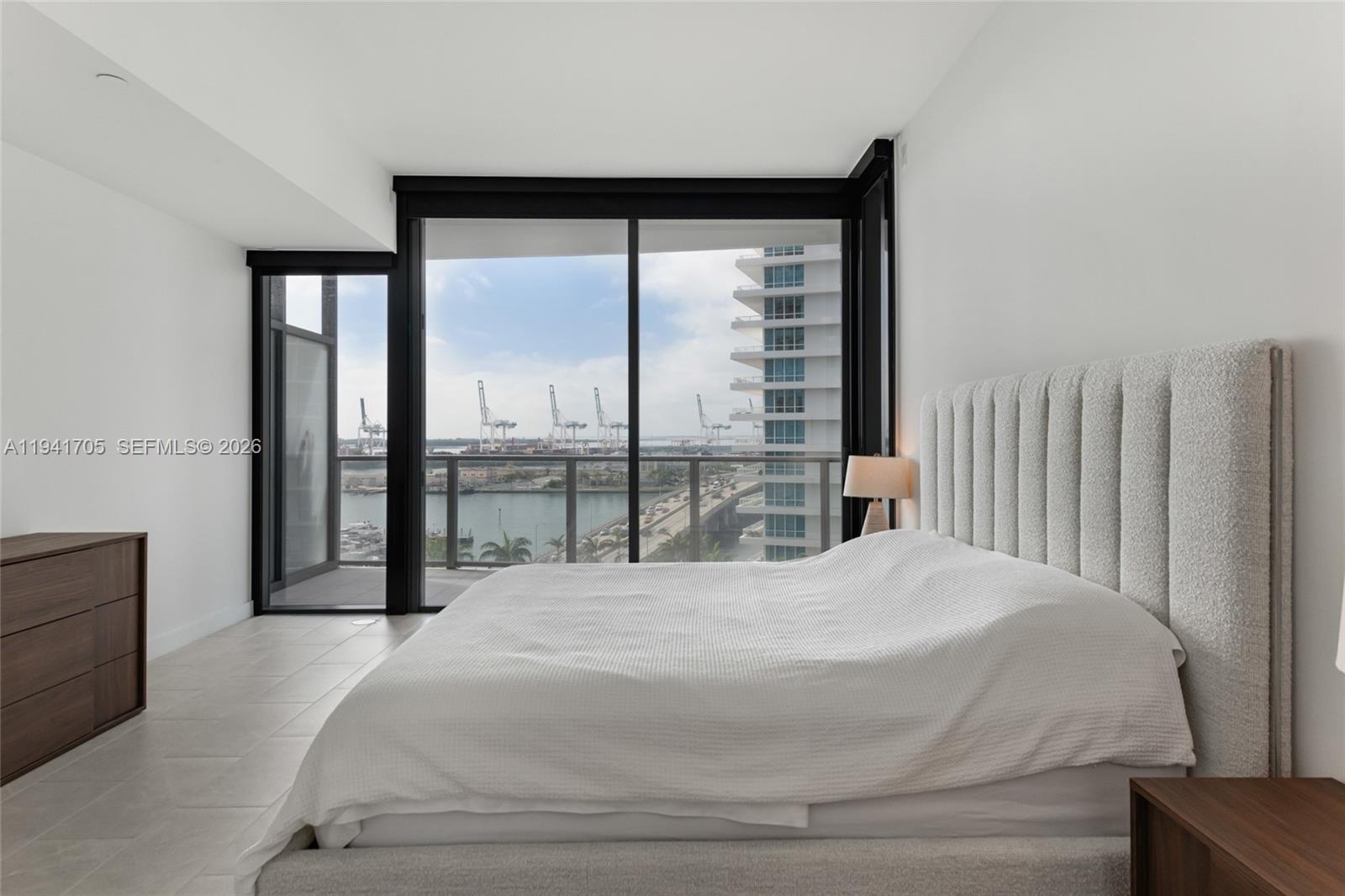 A modern bedroom features a textured headboard, tile floors, and a balcony overlooking a harbor — 500 Alton Rd # 1204, Miami Beach FL 33139, MIAMI BEACH, FL