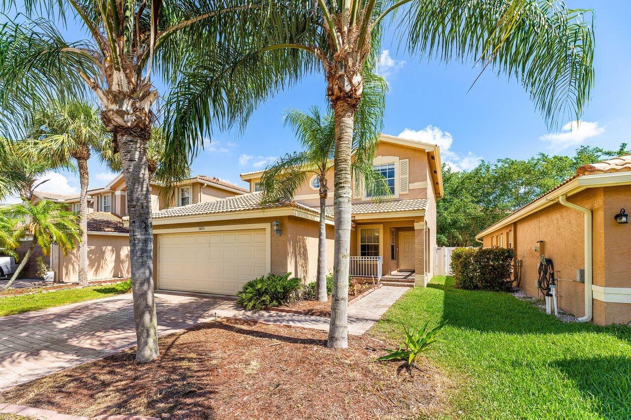 A two-story tan stucco house with a two-car garage and palm trees in the front — 5453 Queenship Court, FL 33463, FL