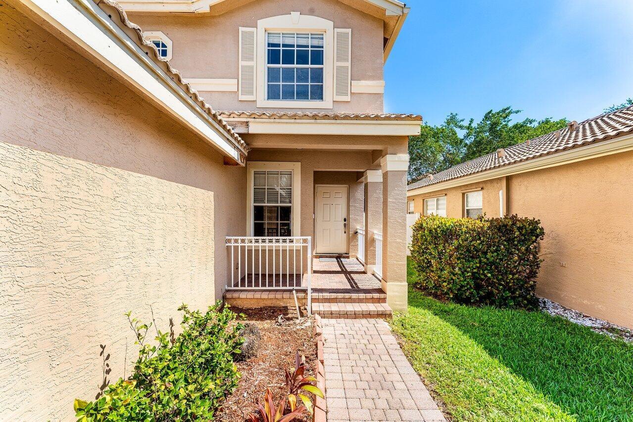 A beige two-story house exterior features a brick walkway leading to a covered front entrance — 5453 Queenship Court, FL 33463, FL