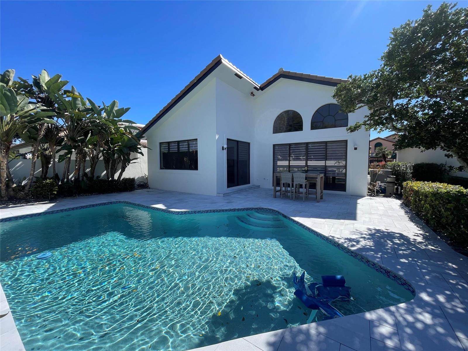 A white house with a swimming pool, patio furniture, and palm trees under a blue sky — 6488 Via Rosa, Boca Raton FL 33433, BOCA RATON, FL