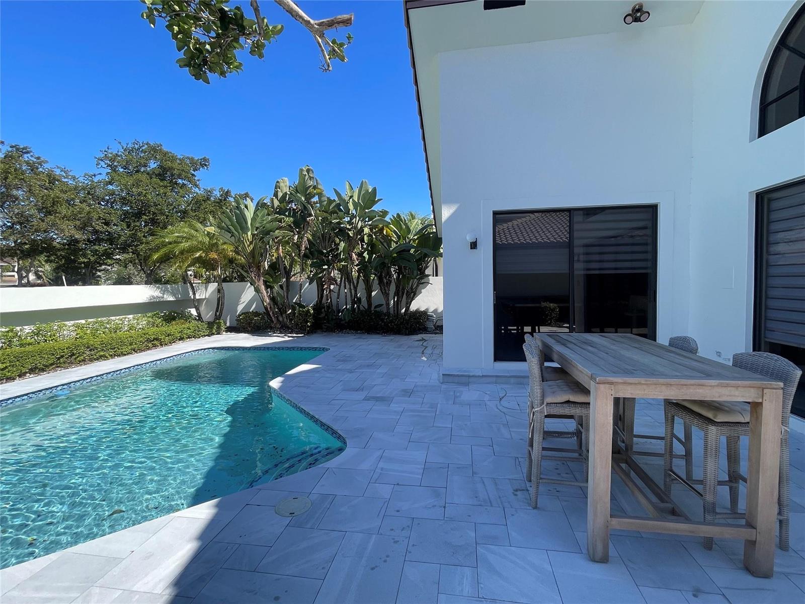 A backyard patio features a swimming pool, a wooden dining set, and tropical landscaping — 6488 Via Rosa, Boca Raton FL 33433, BOCA RATON, FL