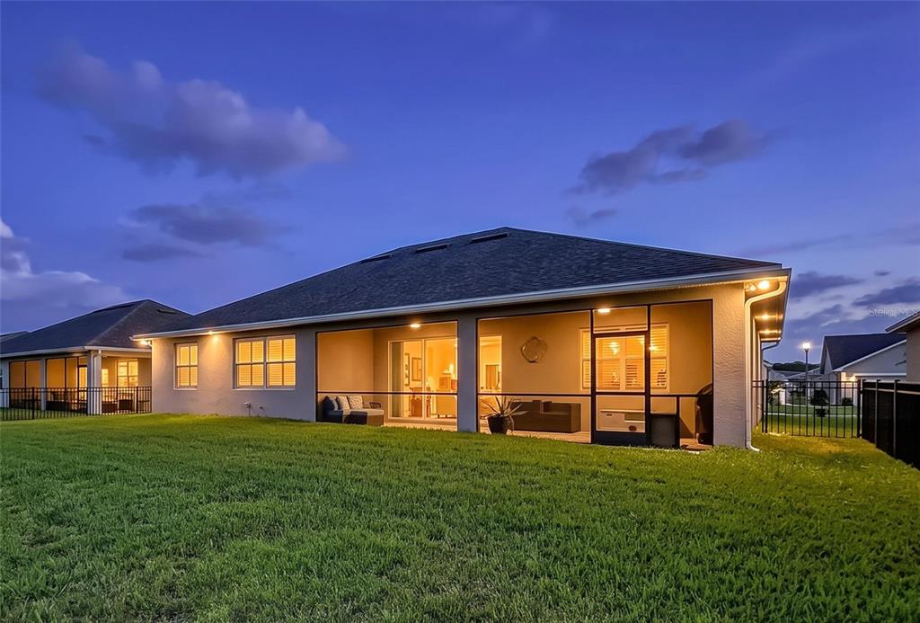 The rear exterior of a single-story house with a screened-in patio and a grassy lawn — 6104 HIGHLANDS GRACE BOULEVARD, LAKELAND, FL