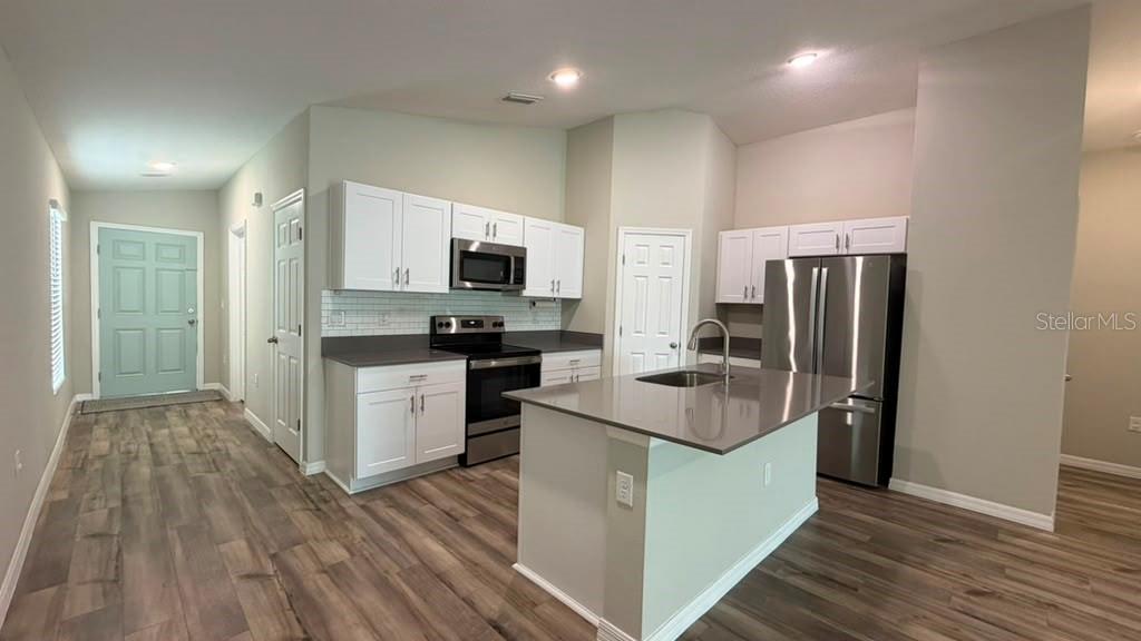 A kitchen features white cabinets, stainless steel appliances, a center island, and wood-look flooring — 4904 MAINSAIL STREET, HAINES CITY, FL