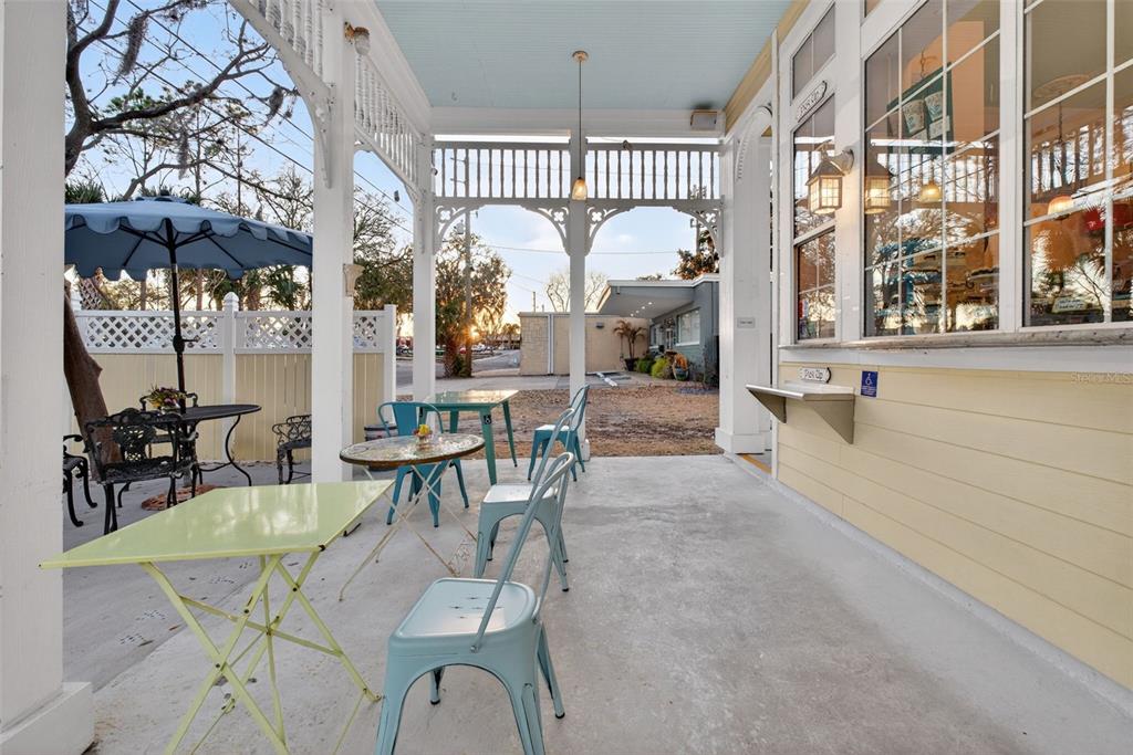 A covered outdoor patio features several small tables and chairs beside a yellow building — 197 E CHURCH STREET, DELAND, FL