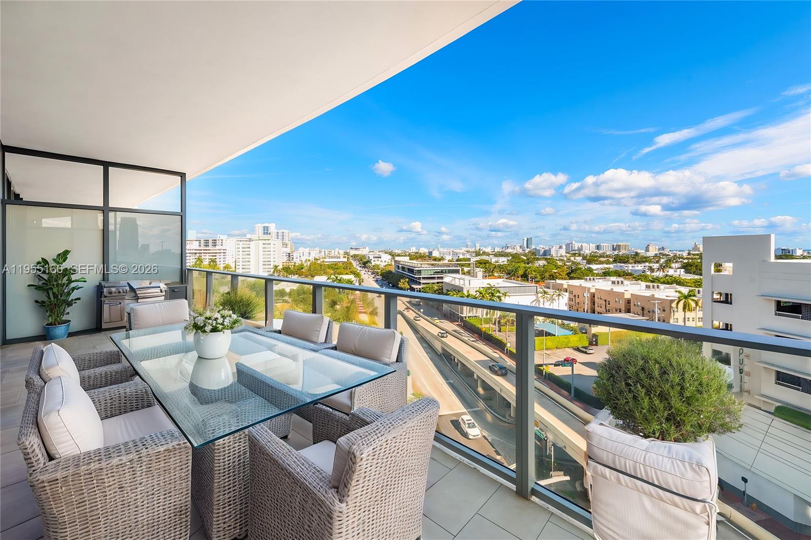 A balcony features a glass-top dining table with wicker chairs overlooking a city highway — 500 Alton Rd # 908, Miami Beach FL 33139, MIAMI BEACH, FL