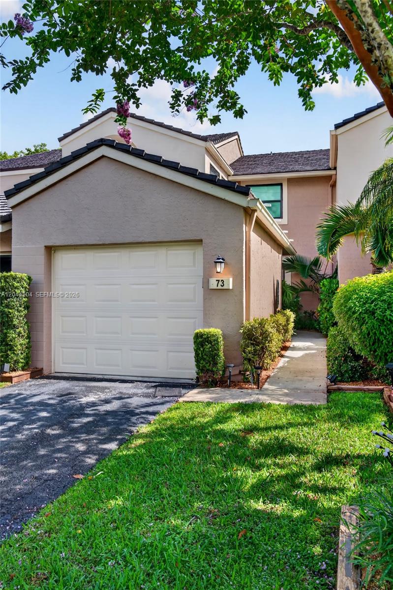 A beige townhouse exterior features a single-car garage, a paved walkway, and lush landscaping — 73 NW 98th Ter, Plantation FL 33324, PLANTATION, FL