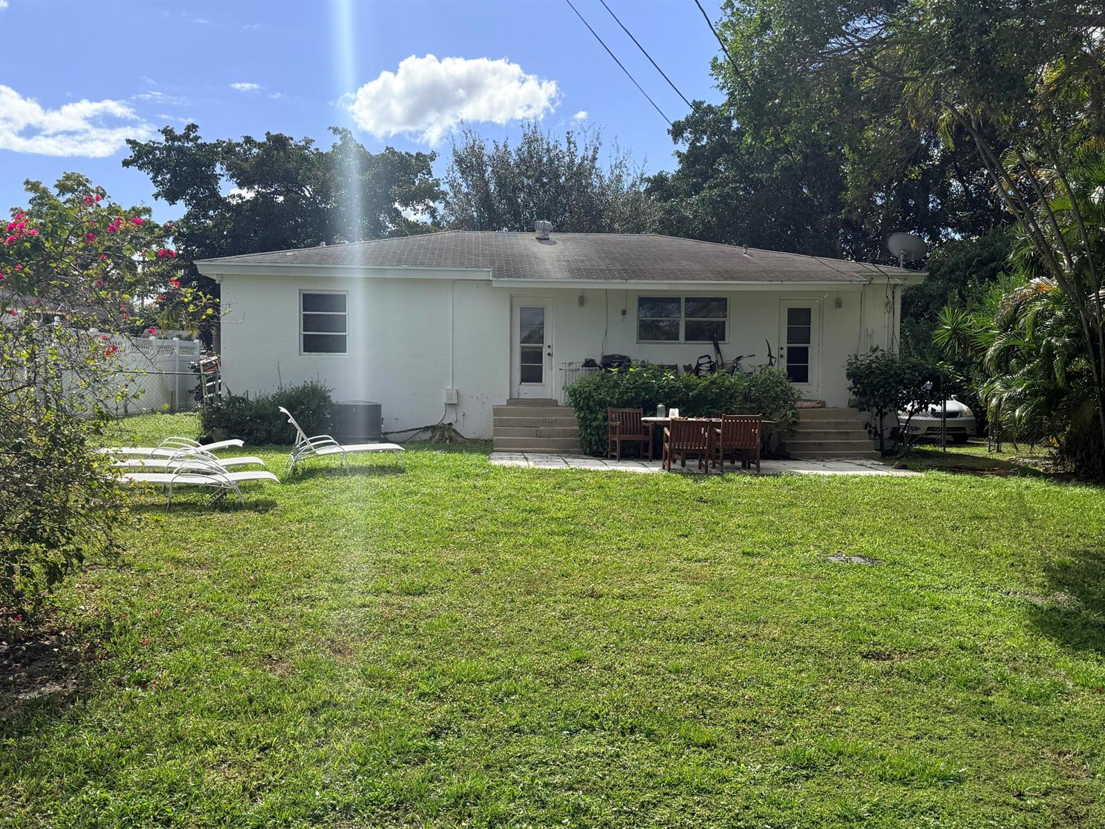 The exterior of a white, single-story house features a grassy backyard, patio furniture, and landscaping — 937 Upland Road, West Palm Beach FL 33401, WEST PALM BEACH, FL