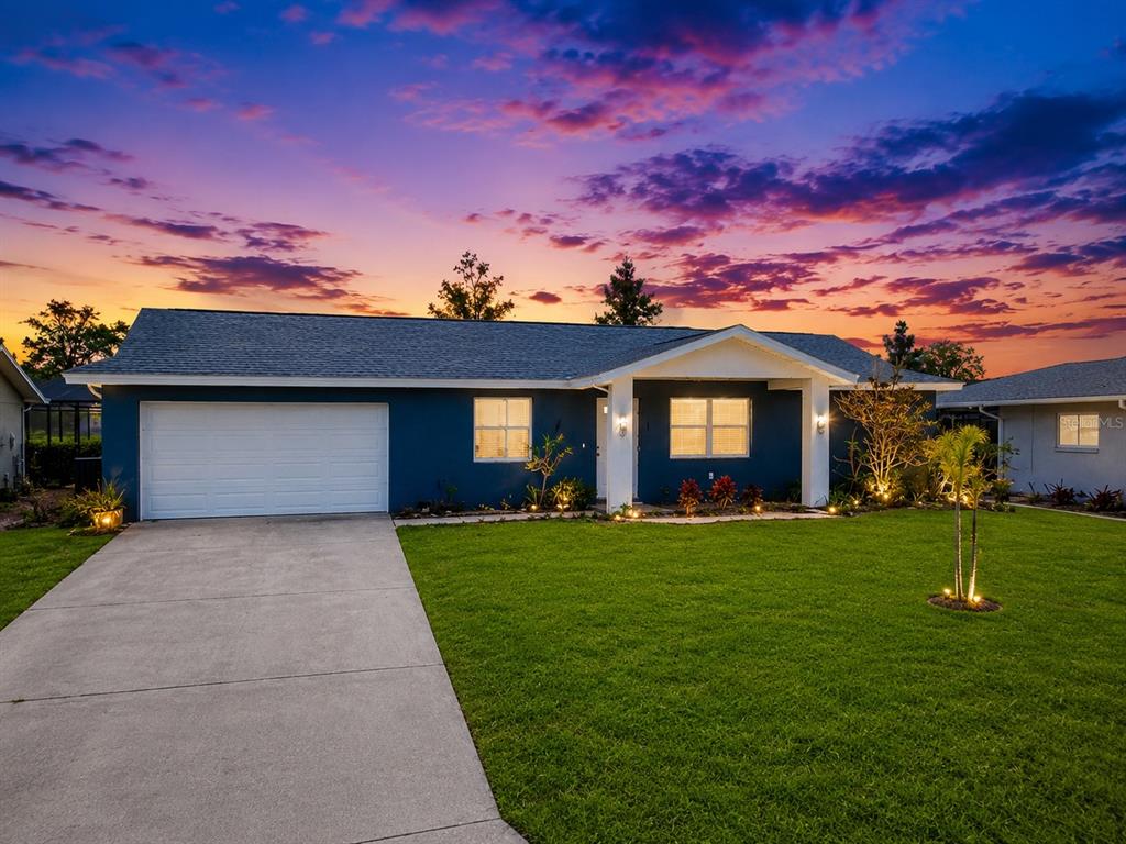 A blue single-story house with a white garage door and a concrete driveway at sunset — 144 ROTONDA CIRCLE, ROTONDA WEST, FL