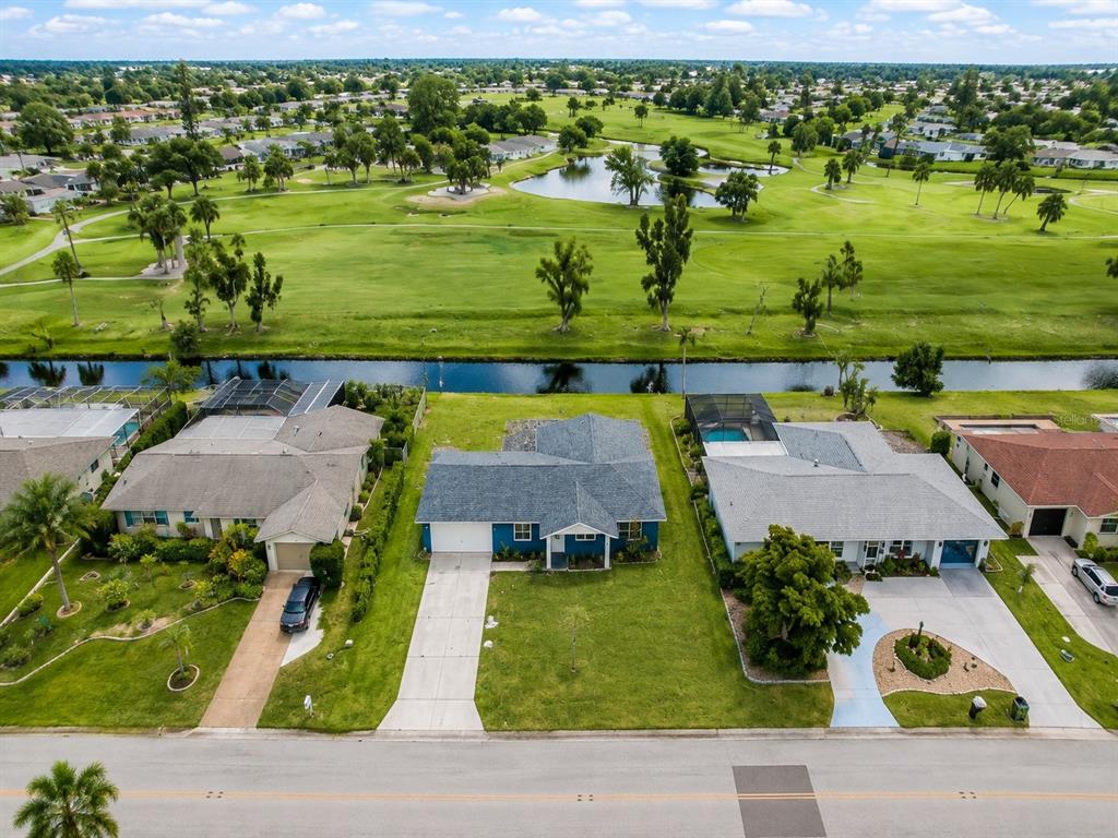 An aerial view shows three suburban houses along a road, facing a canal and golf course — 144 ROTONDA CIRCLE, ROTONDA WEST, FL