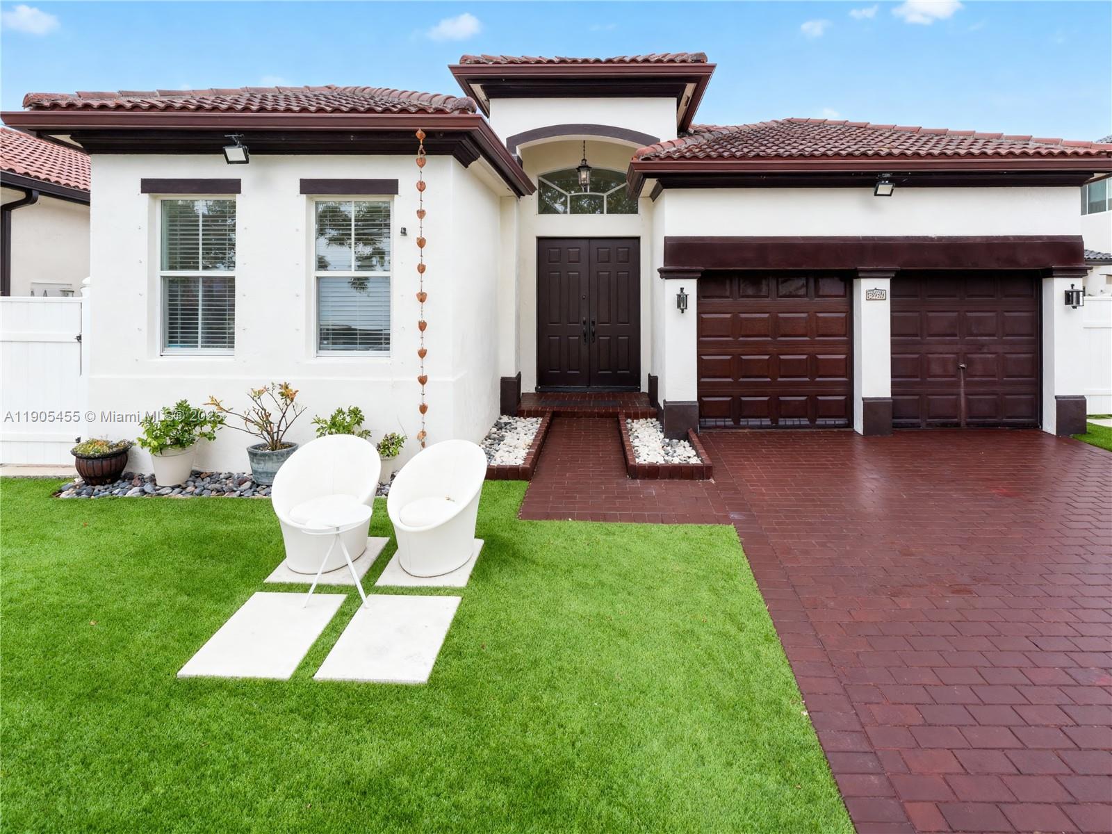 The exterior of a single-story house features a brick driveway, two garage doors, and white walls — 18000 NW 90th Pl, Hialeah FL 33018, HIALEAH, FL
