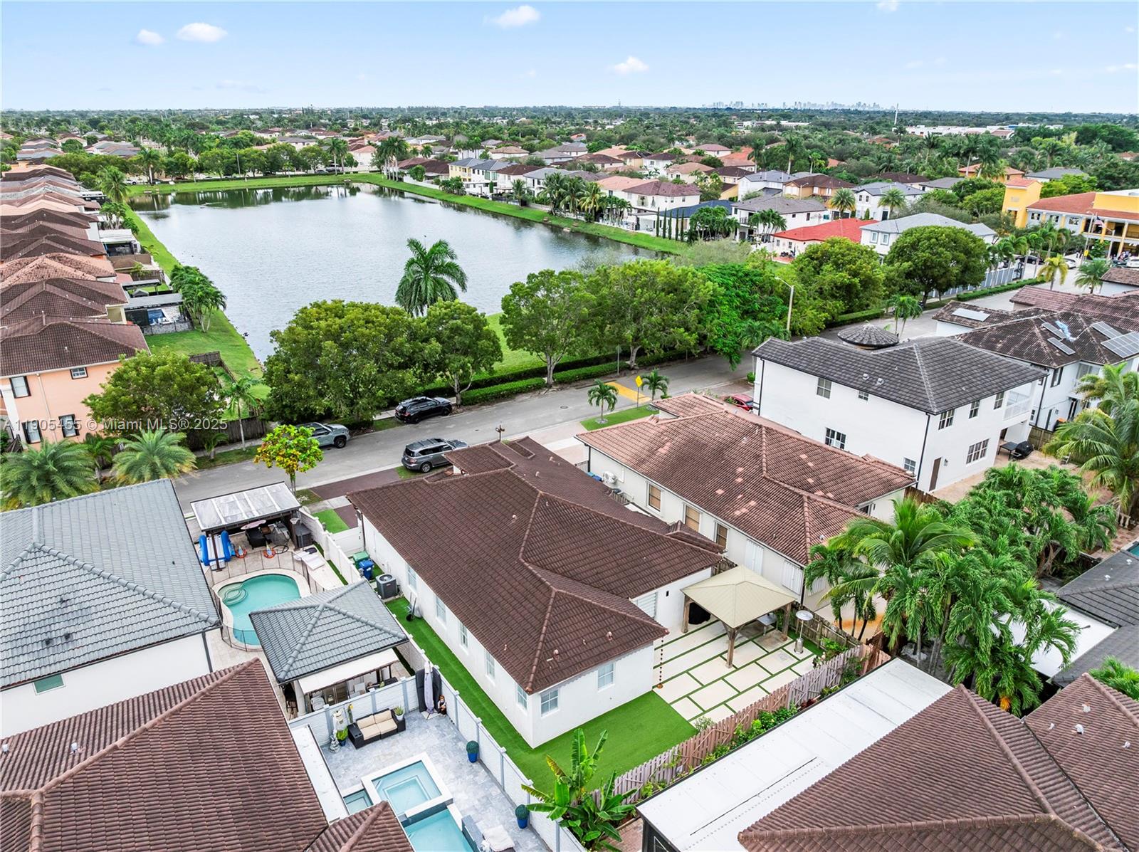 An aerial view shows suburban houses with tiled roofs, swimming pools, and a central lake — 18000 NW 90th Pl, Hialeah FL 33018, HIALEAH, FL