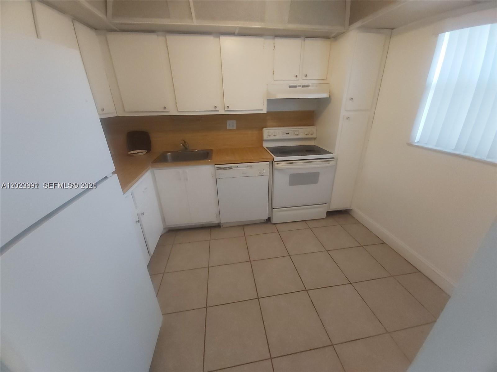 A kitchen features white cabinets, light-colored tile flooring, and white appliances — TAMARAC, FL
