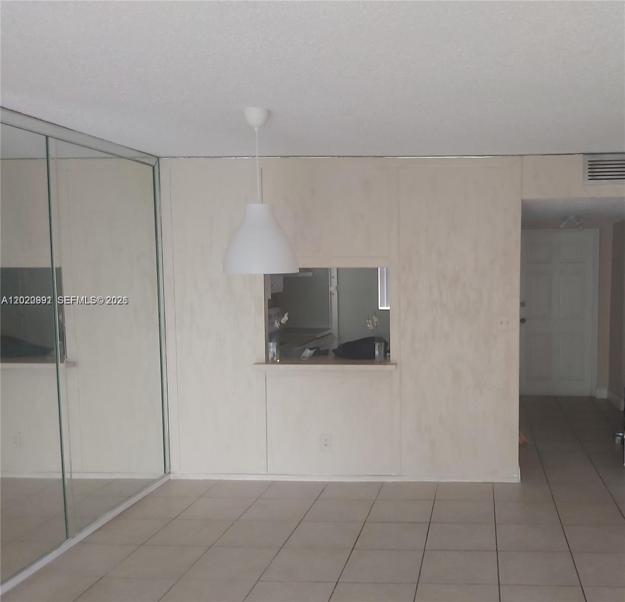 A room with tiled floors, a mirrored wall, a pass-through window, and a pendant light — TAMARAC, FL
