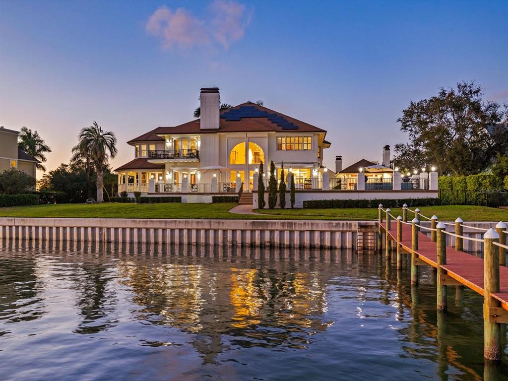 A large waterfront house with a dock, a lawn, and a pool area at dusk — 429 ST ANDREWS DRIVE, BELLEAIR, FL