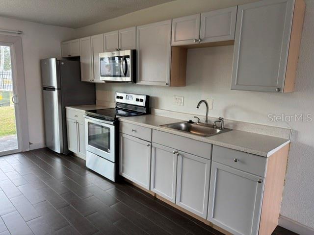 A kitchen features light gray cabinets, stainless steel appliances, and dark wood-look tile flooring — 1883 CARALEE BOULEVARD UNIT 1, ORLANDO, FL