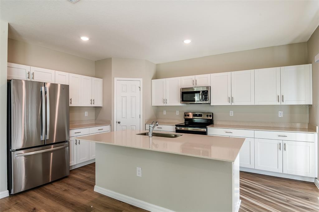 A kitchen with white cabinets, stainless steel appliances, a center island, and wood-look flooring — 33669 NOBLE CREEK PLACE, DADE CITY, FL