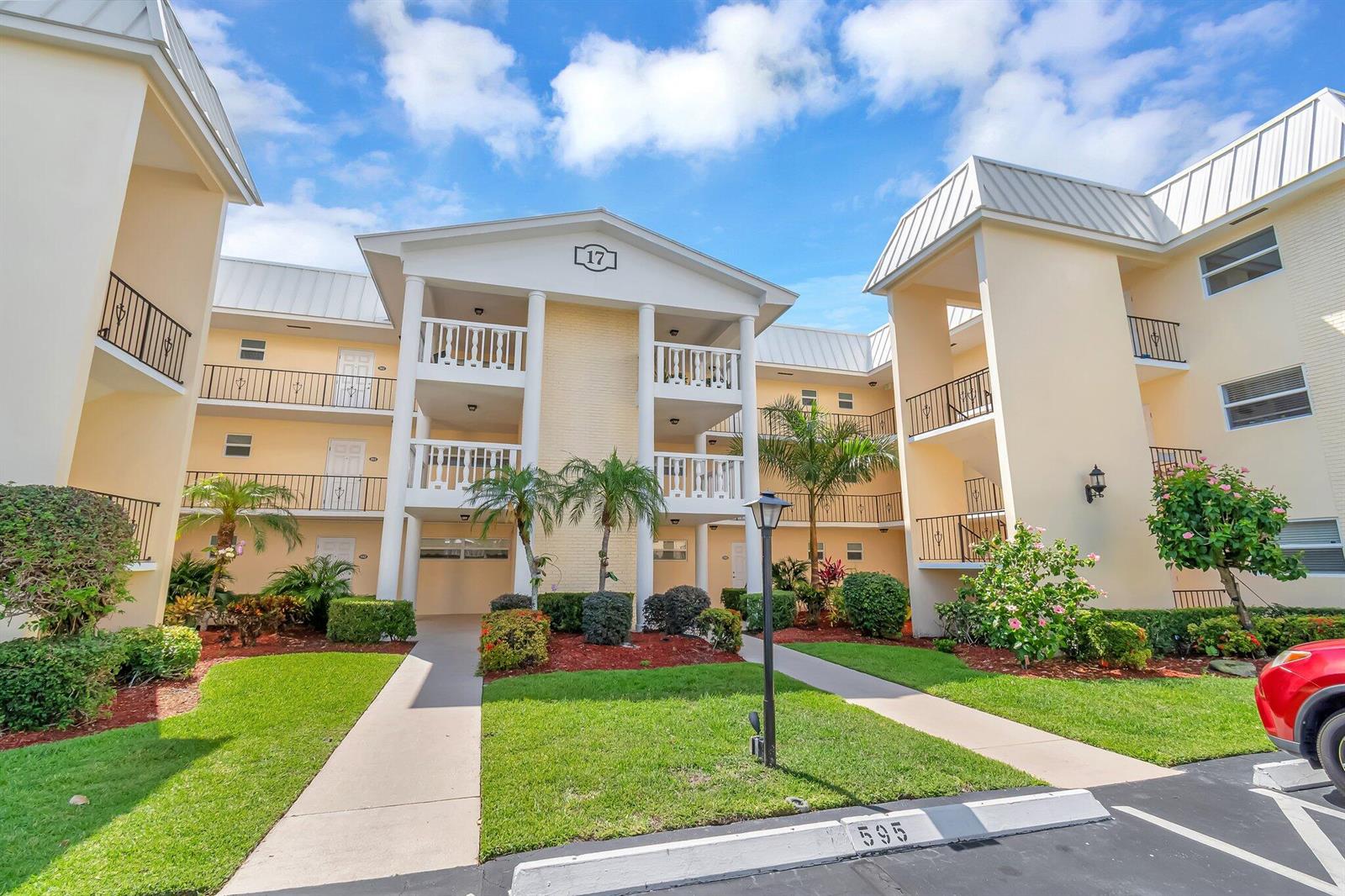 A three-story apartment building with yellow stucco walls, white balconies, and landscaped grounds — 17 Colonial Club Drive # 204, Boynton Beach FL 33435, BOYNTON BEACH, FL